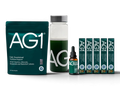 AG1 Daily Foundational Nutrition Support bundle featuring a dark green pouch, a clear bottle with green liquid and white AG1 branding, a small amber dropper bottle, and five slim green boxes, all on a white background.