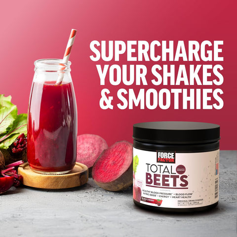 Glass of red shake with a straw, jar of Total Beets powder, and beets on a gray surface with red background.