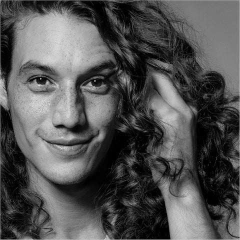 Black and white portrait of a person with curly hair, one hand on their face.