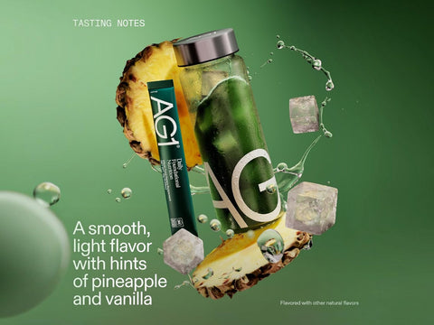 A green AG1 beverage can and matching tube floating with pineapple slices and ice cubes against a green gradient background. Text reads 'TASTING NOTES' and 'A smooth, light flavor with hints of pineapple and vanilla.