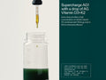 A clear glass supplement bottle with a black dropper above it, shown on a split white and dark teal background with marketing text about Supercharge AG1 and Vitamin D3+K2.
