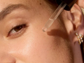 Close-up of a person applying a dropper of liquid to their face.