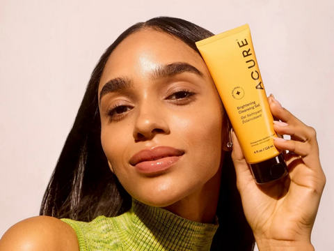 Woman holding a tube of Acure skincare product against a plain background