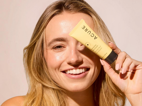 Woman holding a tube of 'Aoure' sunscreen against her face on a plain background