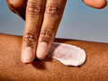 Hand applying cream to a person's arm with a blurred background