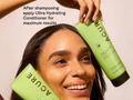 Woman holding two bottles of ACURE Ultra Hydrating Conditioner with text on a beige background