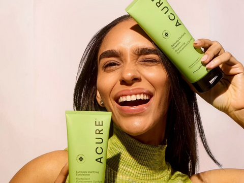 Woman holding two Acure skincare products against a plain background