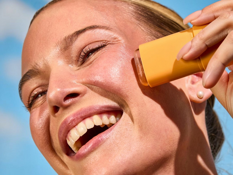 Person applying sunscreen to their face with a yellow bottle against a blue sky.