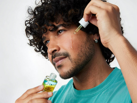 Man applying a dropper of oil to his face with a bottle of oil in his other hand.