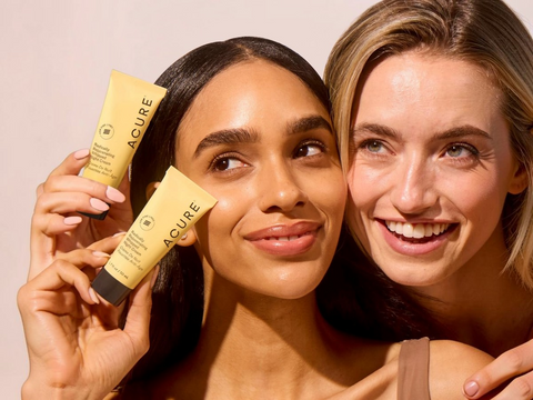 Two women holding Acure skincare products against a beige background