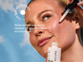 Woman applying sunscreen with a dropper bottle against a blue sky background