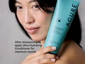 Woman holding a bottle of Acure Ultra Hydrating Conditioner with text on a gray background