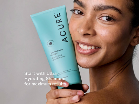 Woman holding a bottle of Acure Ultra Hydrating Shampoo against a neutral background