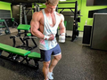Muscular man in a gym holding a protein supplement container.