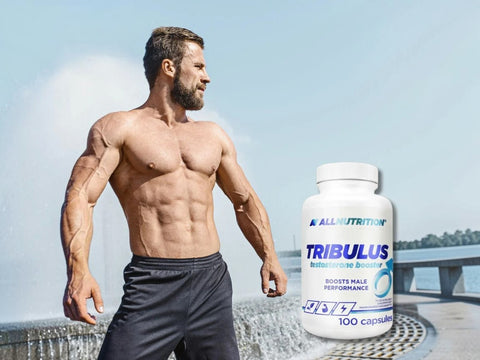 Muscular man holding a supplement bottle labeled 'TRIBULUS' by AllNutrition against a clear sky.