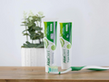 AloeDent toothpaste and toothbrush on a wooden surface with a plant in the background