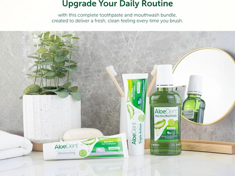 AloeDent toothpaste, mouthwash, and toothbrush on a bathroom counter with a plant and mirror in the background.