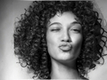 Black and white portrait of a woman with curly hair blowing a kiss.