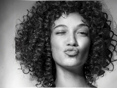 Black and white portrait of a woman with curly hair blowing a kiss.