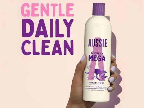 Aussie Mighty Mega shampoo bottle held by a hand with text 'Gentle Daily Clean' on a pink background