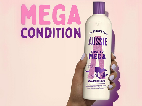 Aussie Mighty Mega conditioner bottle held by a hand with a pink background and 'Mega Condition' text.