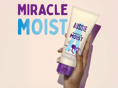 Aussie Miracle Moist conditioner bottle held by a hand with a pink background and text.