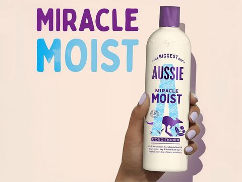 Aussie Miracle Moist conditioner bottle held in a hand with text on a beige background