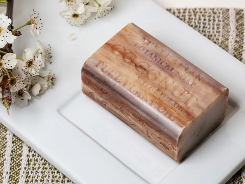 Bar of soap with 'Botanic' branding on a white surface with flowers.