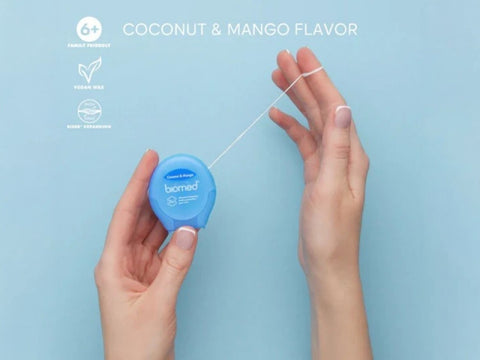 Close-up of BIOMED Coconut and Mango flavoredfloss stretched between fingers.