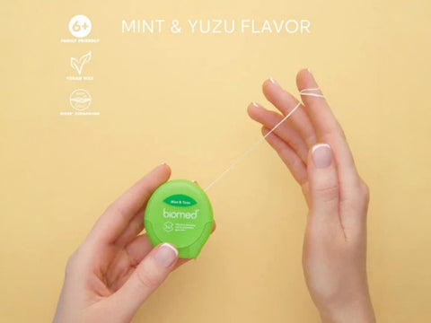 Close-up of BIOMED green and white floss stretched between fingers.
