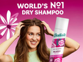 Woman holding Batiste dry shampoo with pink background and text claiming it's 'World's No.1'.