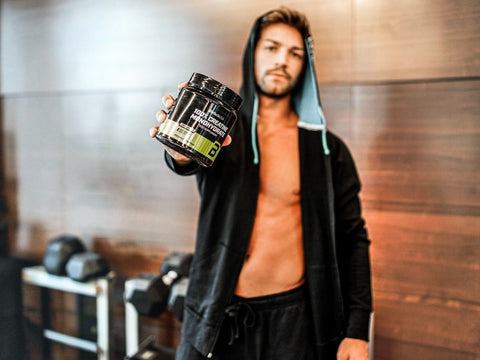 Man holding a supplement container in a gym setting