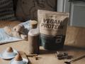 Bag of vegan protein powder on a table with eggs, bread, and spices.