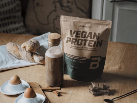 Bag of vegan protein powder on a table with eggs, bread, and spices.