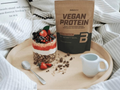 Vegan protein package on a wooden tray with a layered dessert and small pitcher.