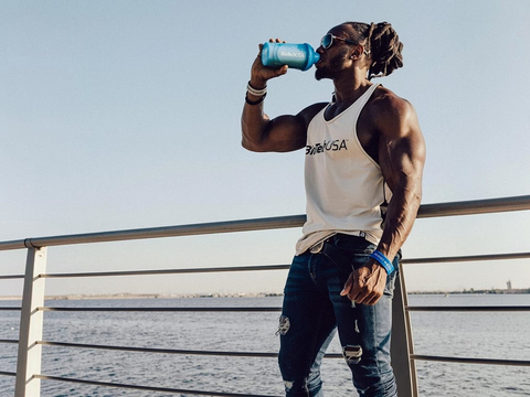 Man drinking from a blue water bottle by a waterfront