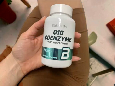 Hand holding a bottle of BioTechUSA Q10 Coenzyme food supplement.