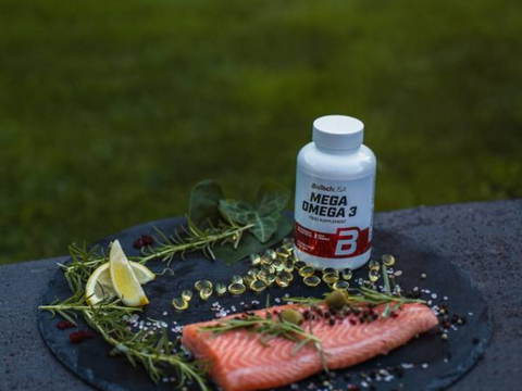 Bottle of Mega Omega 3 supplement with salmon and herbs on a dark surface