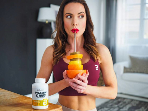 Woman holding a layered fruit drink with a vitamin C supplement bottle on a table.