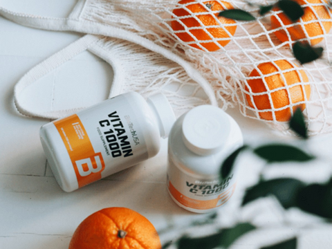 Two bottles of vitamin C supplements on a surface with oranges and a checkered cloth in the background.