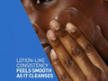 Close-up of a person's hand applying lotion to their face with a blue background and text about lotion-like consistency.