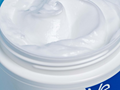 Close-up of a white cream jar with a blue logo on a white background