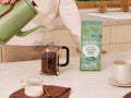 How to Use: Four Sigmatic ground coffee being scooped next to a coffee maker.