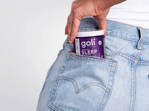 Person putting a Goli Sleep supplement container into their jeans pocket on a white background