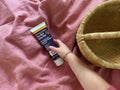 Hand holding a tube of Derma-Lotion on a pink surface with a woven basket.