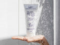 Hand holding a bottle of 'Dry, Itchy Flaky Scalp' treatment under running water.
