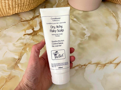 Hand holding a tube of Hope's Relief conditioner on a marble surface
