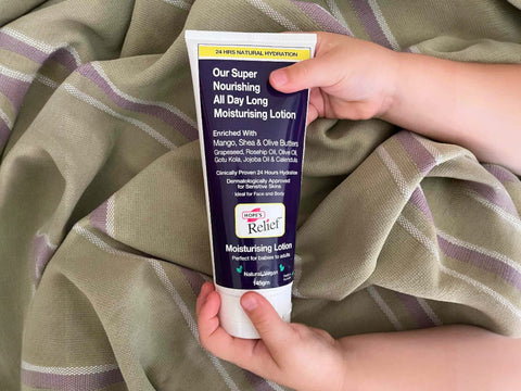 Hand holding a tube of moisturizing lotion with a checkered fabric background