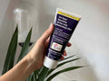 Hand holding a tube of L'Occitane Relief Moisturising Lotion with a plant in the background