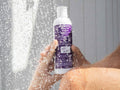 Person holding a bottle of shampoo under running water